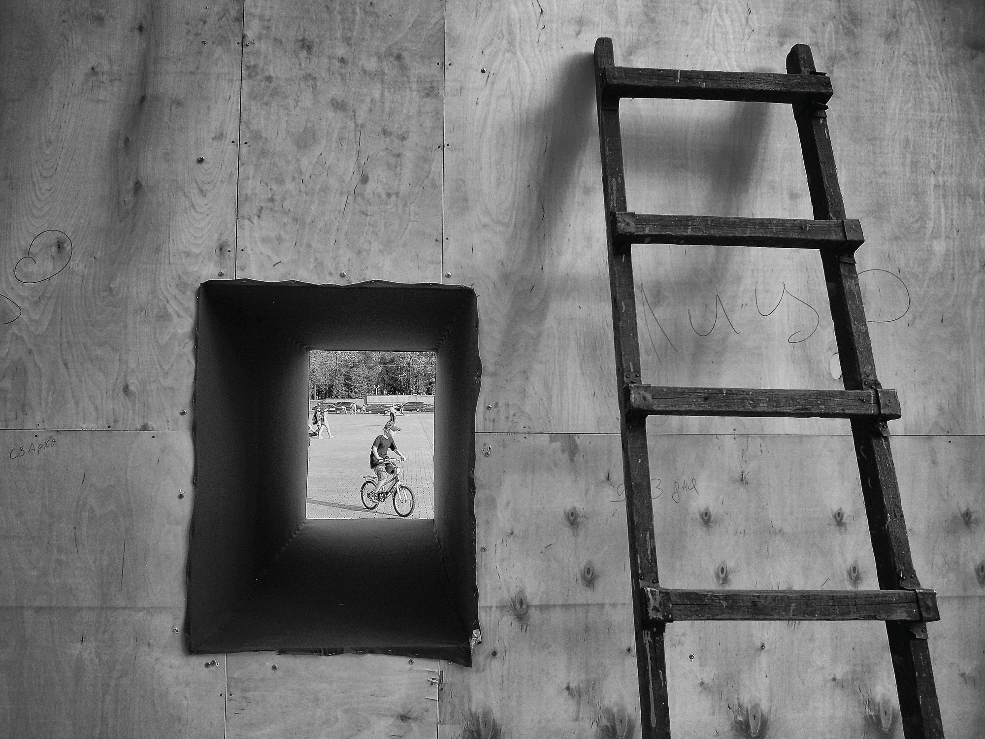 A ladder beside a square opening in a wooden wall, a cyclist framed inside